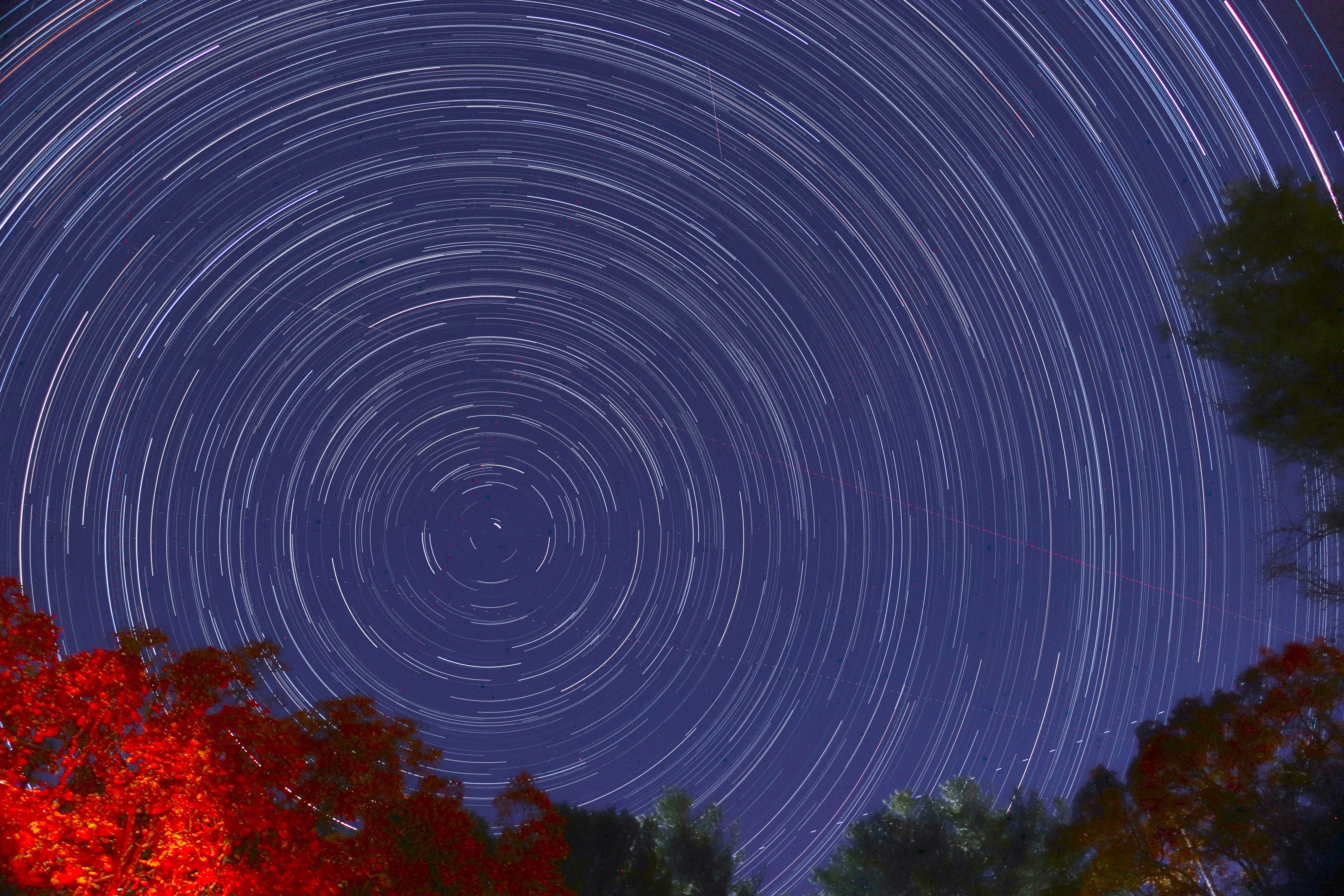 This image was created by pointing a camera at the North Celestial Pole (NCP) and capturing 192 consecutive images. The images were then put together using software called StarStaX. Because we captured so many images we are able to see the Earth’s rotation which is centered about the NCP. This process created the star trails you see in this image. Slightly offset from the center to the lower left is the north star, Polaris, which is very close to the Celestial Pole. 
If you look carefully you can see some plane and satellite trials, and even a small meteor, cutting across the star trails.